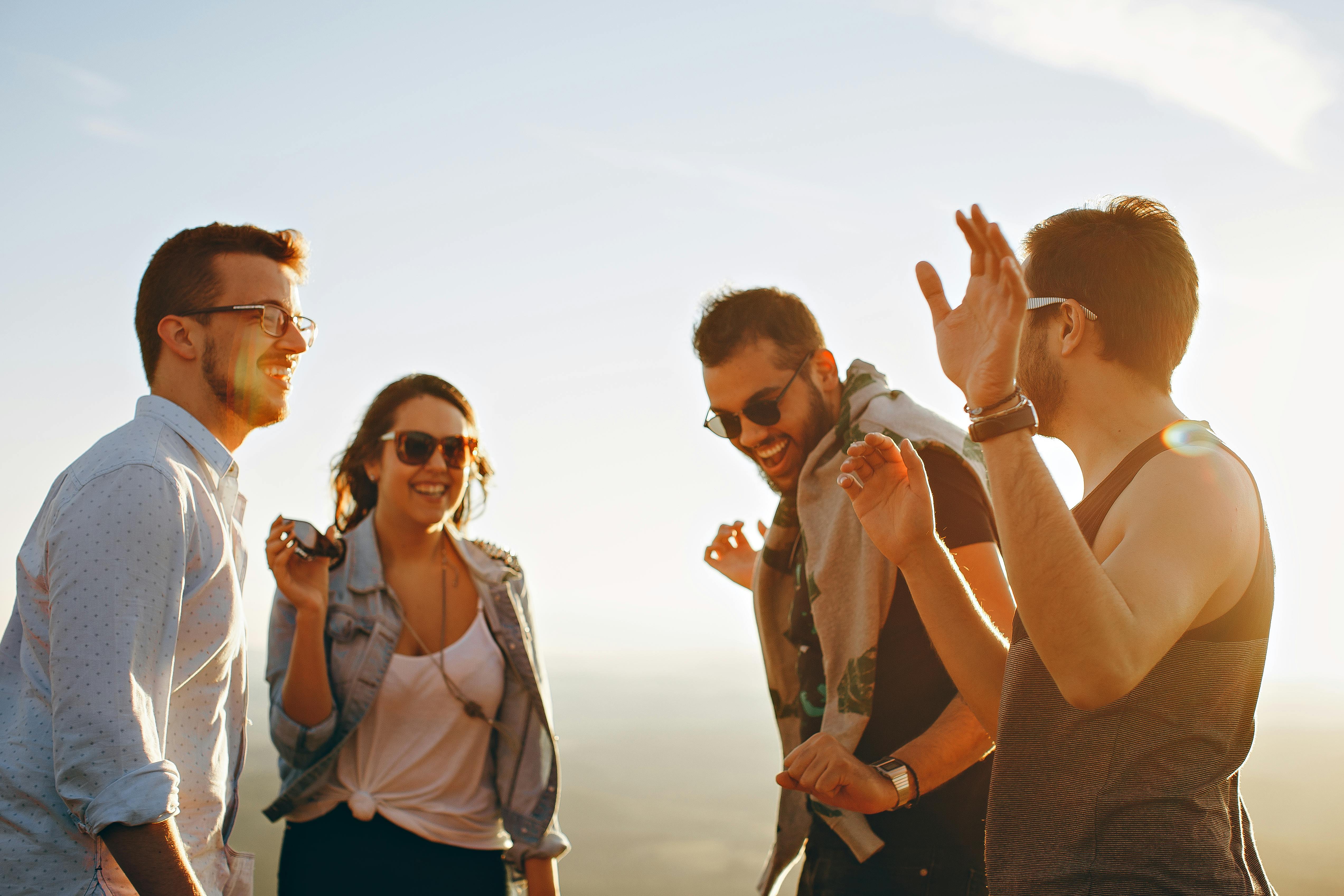 a group of four young people standing outdoors, smiling and dancing